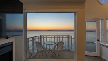 Ein Balkon mit Meerblick bei Sonnenuntergang, ein runder Tisch und zwei Stühle.