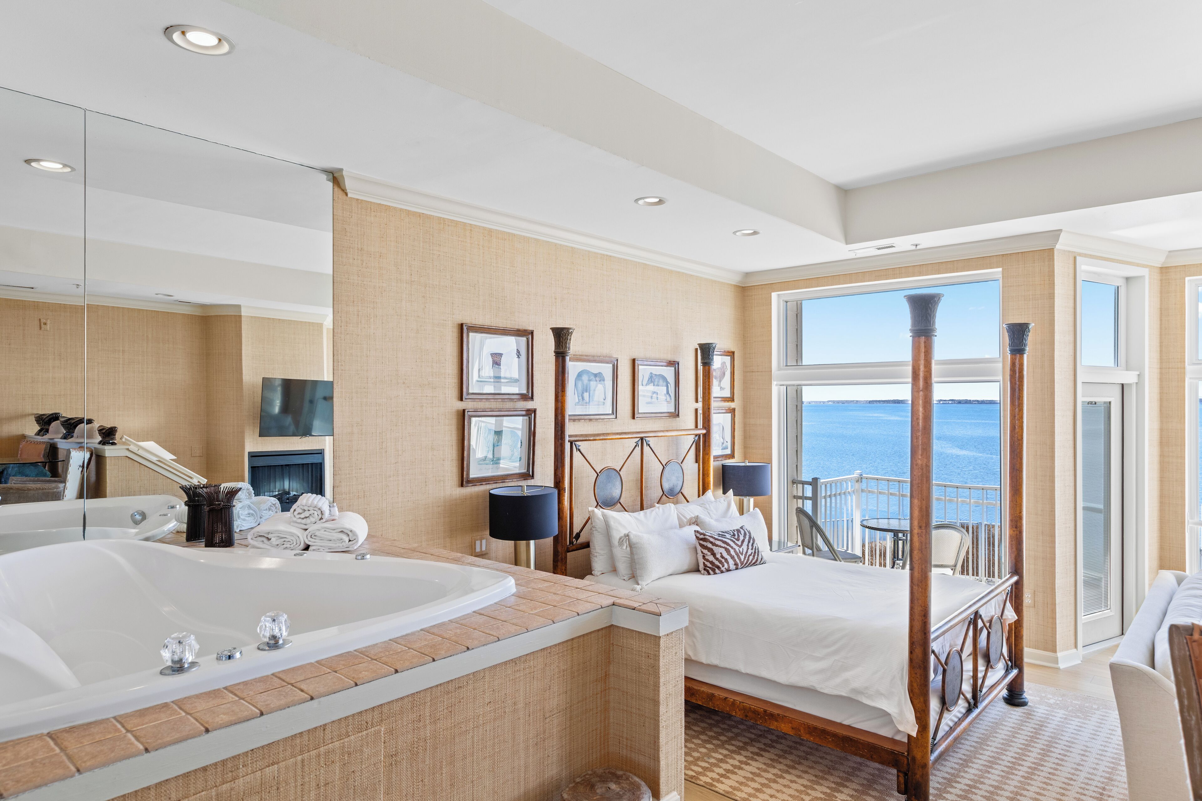 Un dormitorio amplio con una bañera grande, una cama con dosel y un balcón con vista al mar.