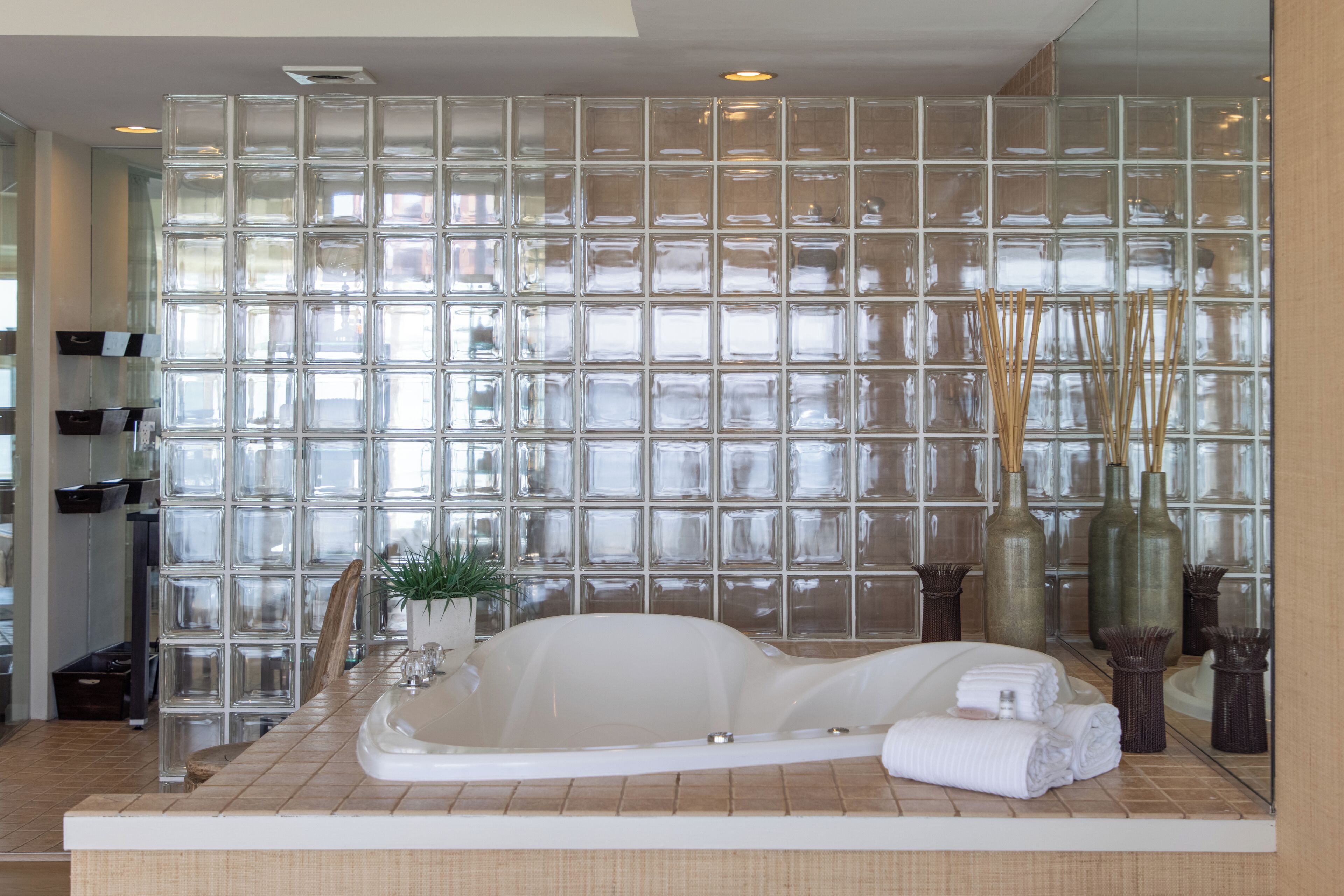 A modern bathroom with a glass block wall, a freestanding bathtub, and a mirror reflecting the room.