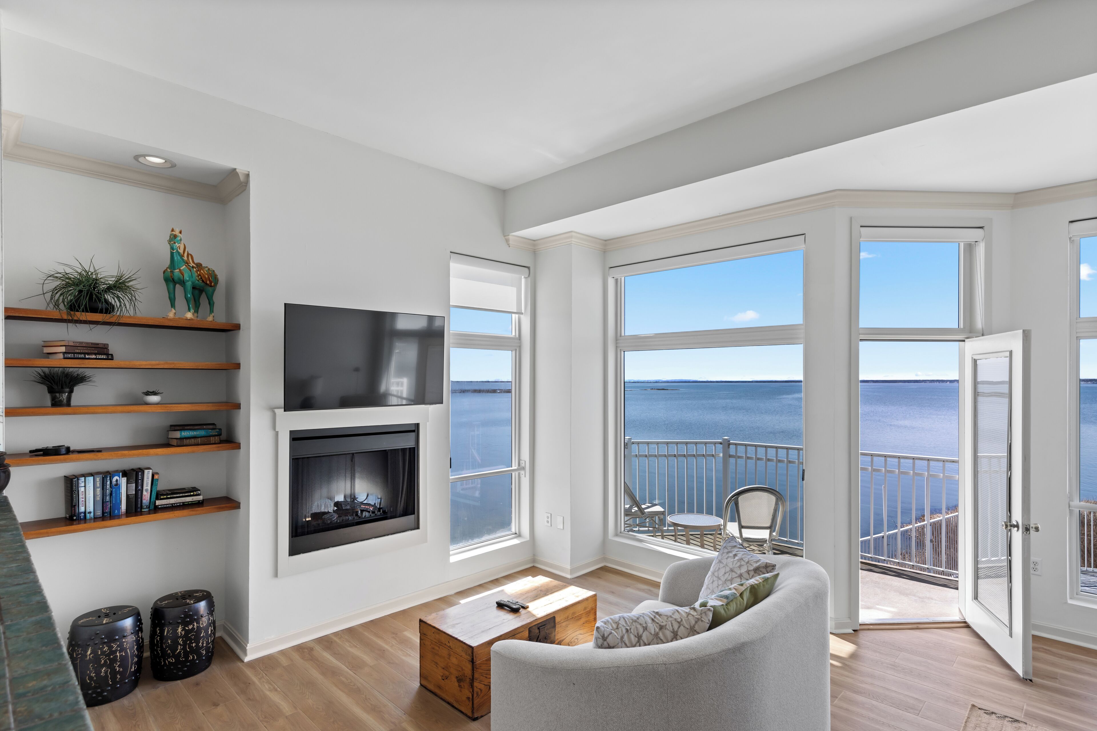 A spacious living room with a fireplace, large windows, and a balcony with a view of the sea.