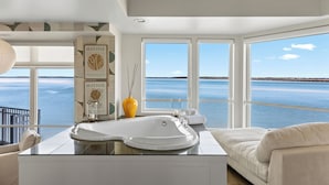 A modern bathroom with a large bathtub, a white sink, and a view of the sea through large windows. - The Edge at Fager's Island (Ocean City)