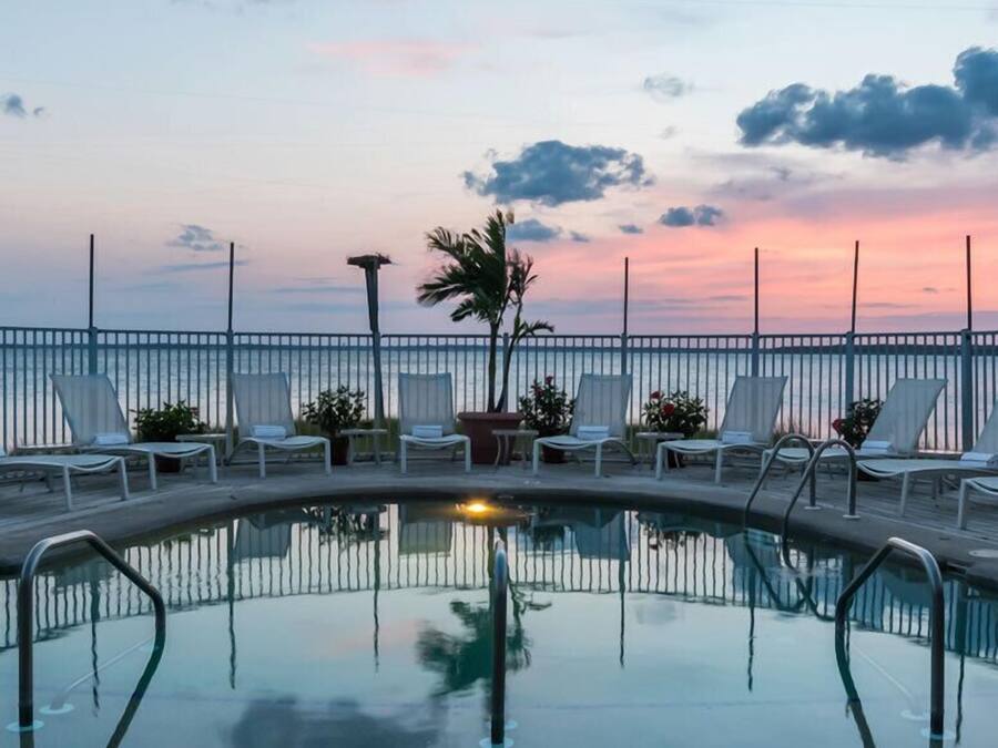 A poolside area with lounge chairs and a palm tree, surrounded by a railing, during sunset.