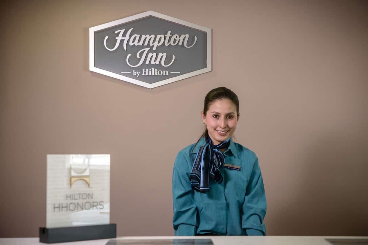 Una recepción de hotel con un letrero que dice 'Hampton Inn by Hilton' y otro letrero debajo que indica 'Hilton HHONORS'.