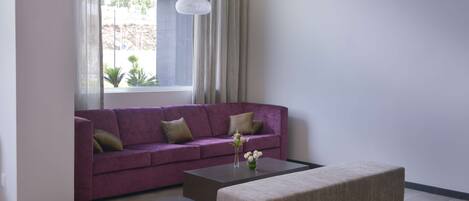 A modern living room with a purple sofa, a beige ottoman, and a coffee table with a vase of flowers.