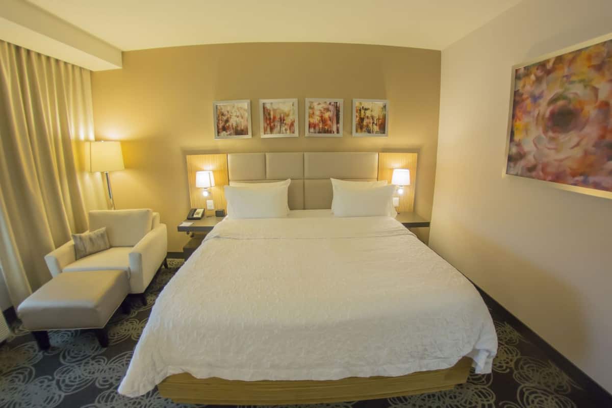 Una habitación de hotel con una cama, dos mesitas de noche, una silla, un escritorio, un teléfono y una ventana con cortinas.