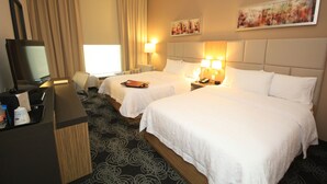 A hotel room with two beds, a desk with a computer, a TV, and a window with curtains.