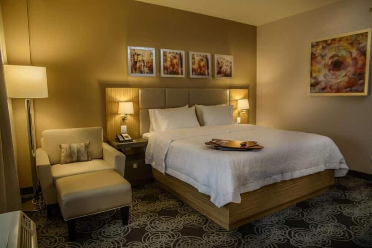 Habitación de hotel con cama, una silla, una mesita de noche y una lámpara.