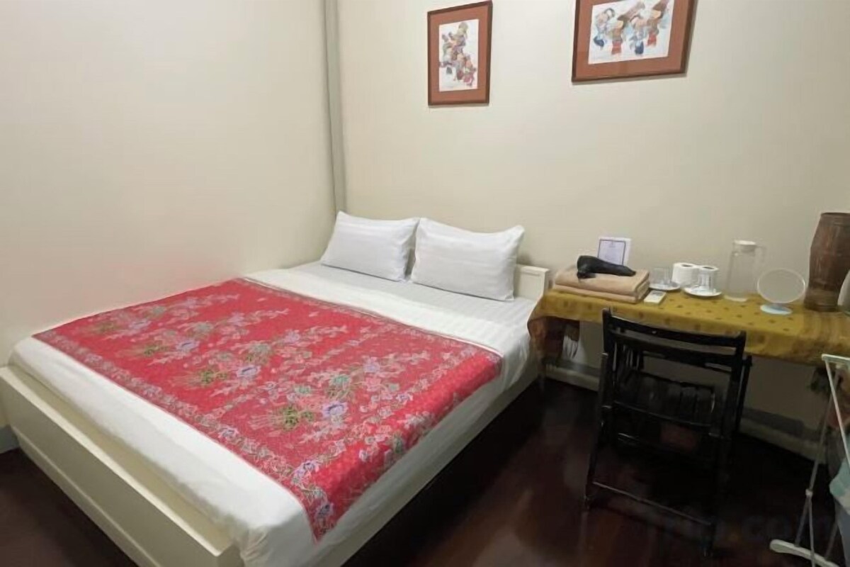 A bedroom with a bed, a desk with a chair, and two framed pictures on the wall.