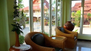 A lobby with wicker furniture, a vase with flowers, and a view of buildings outside. - Sangthong Resort (Saraphi)