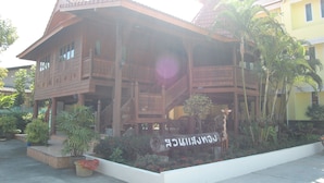 A traditional wooden building with a balcony, surrounded by potted plants and a sign. - Sangthong Resort (Saraphi)