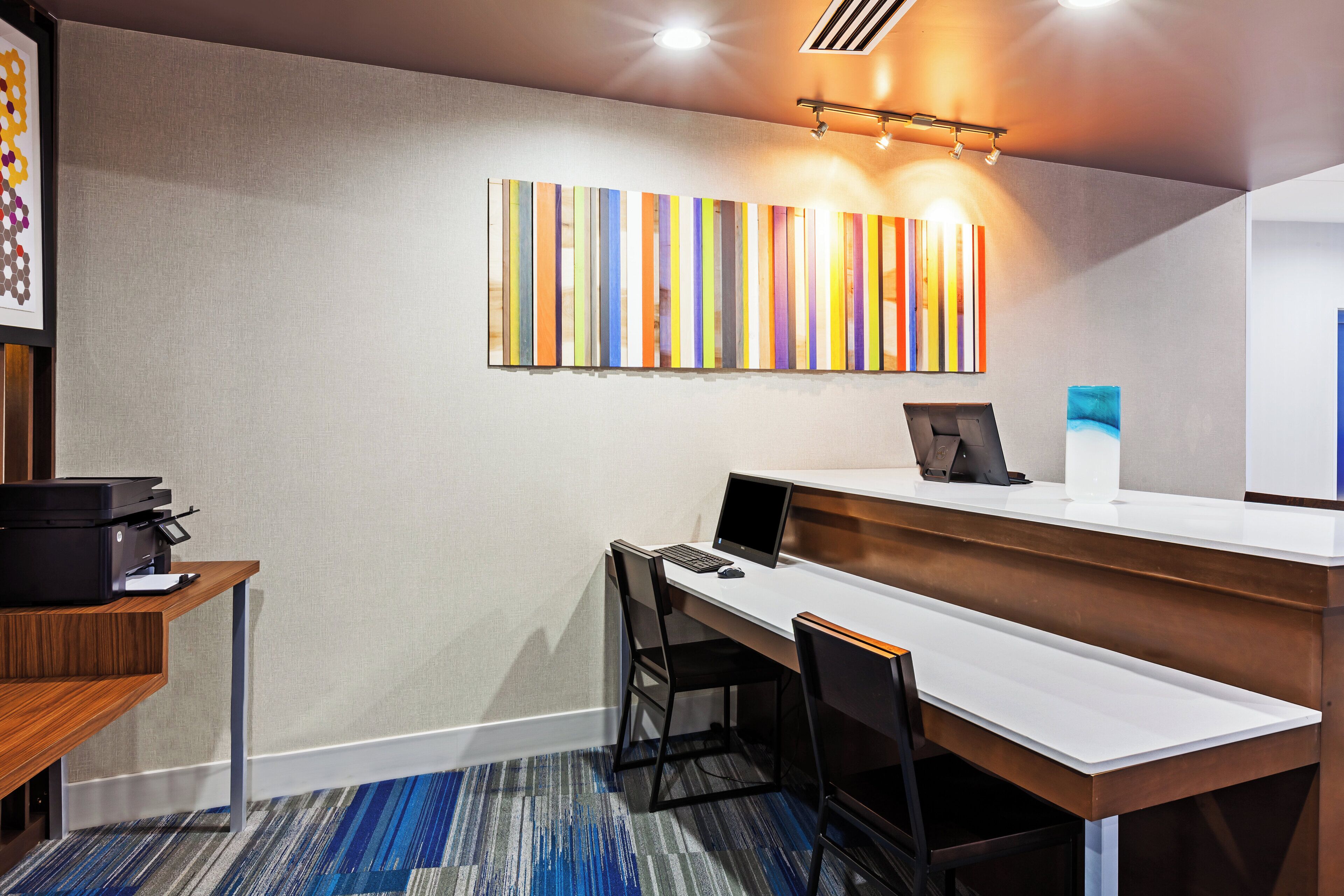 Un espace de bureau moderne comprenant un bureau, des chaises, une imprimante et un tableau abstrait aux couleurs vives accroché au mur.