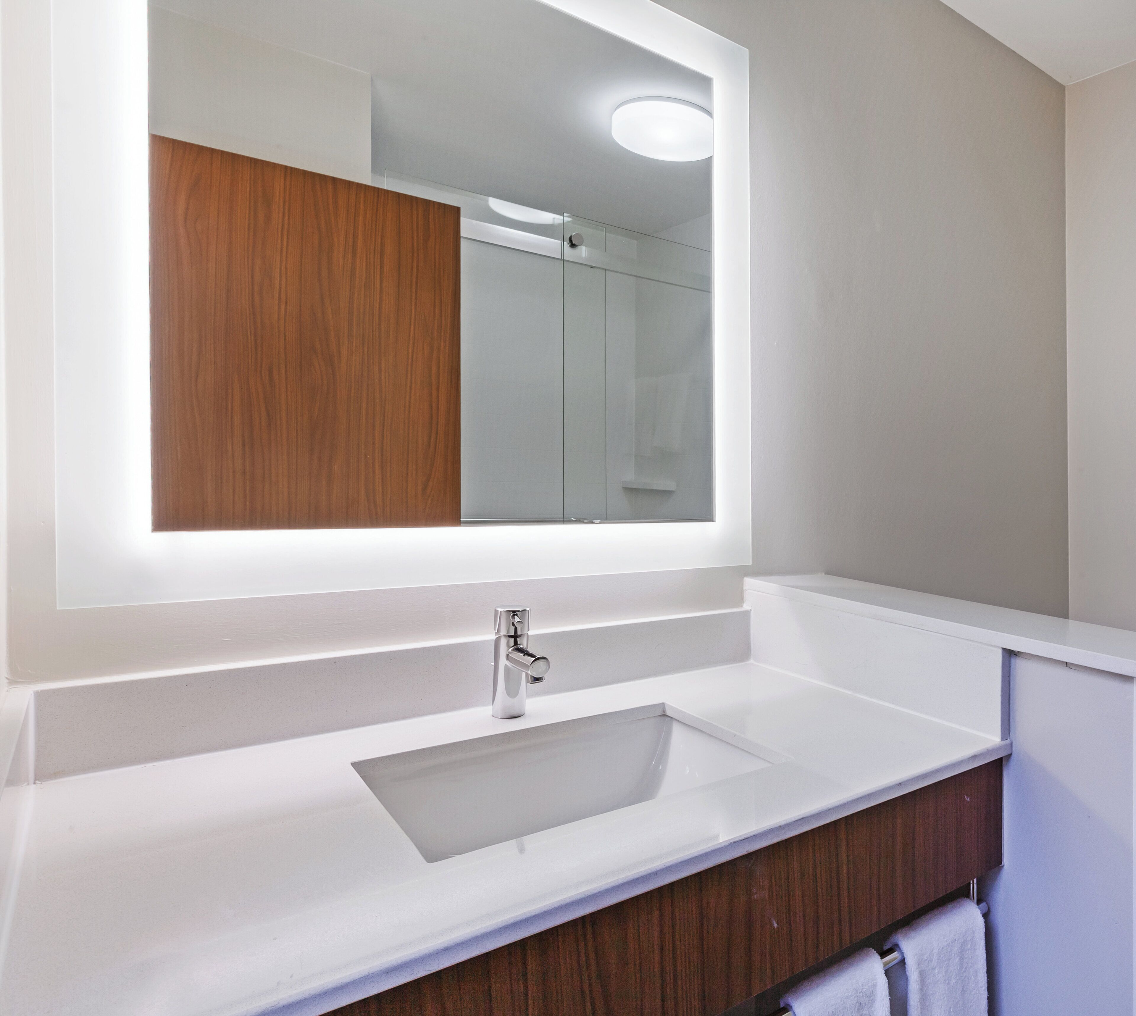 Un baño moderno con un espejo grande, un lavamanos blanco y un mueble de tocador de madera.