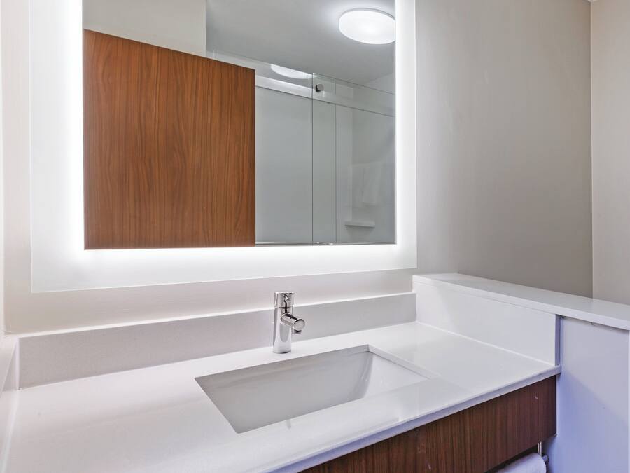 Un baño moderno con un espejo grande, un lavamanos blanco y un mueble de tocador de madera.