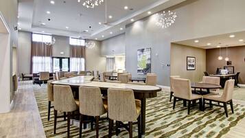 A spacious hotel lobby with multiple seating areas, including a large round table and several smaller tables.