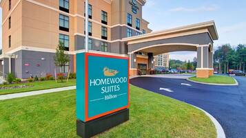 A hotel entrance with a sign for Homewood Suites Hilton, a covered walkway, and a parking area.