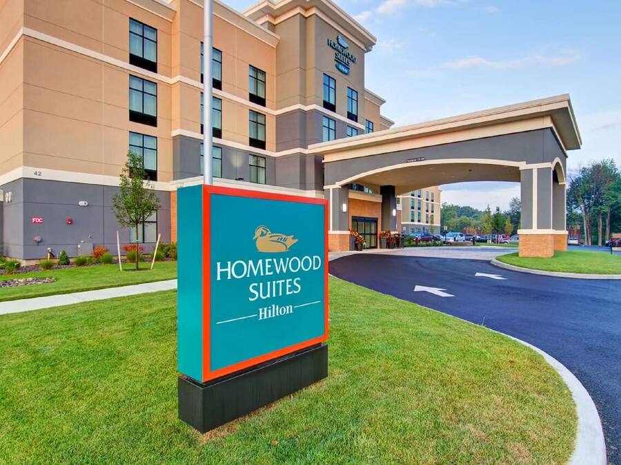 A hotel entrance with a sign for Homewood Suites Hilton, a covered walkway, and a parking area.