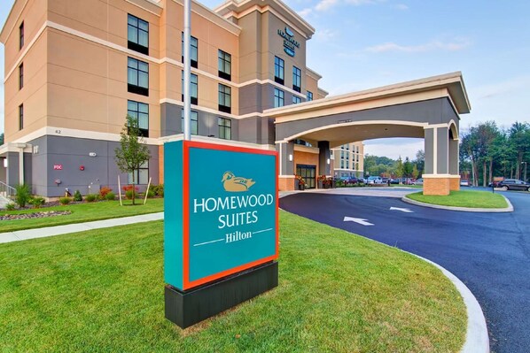 A hotel entrance with a sign for Homewood Suites Hilton, a covered walkway, and a parking area.
