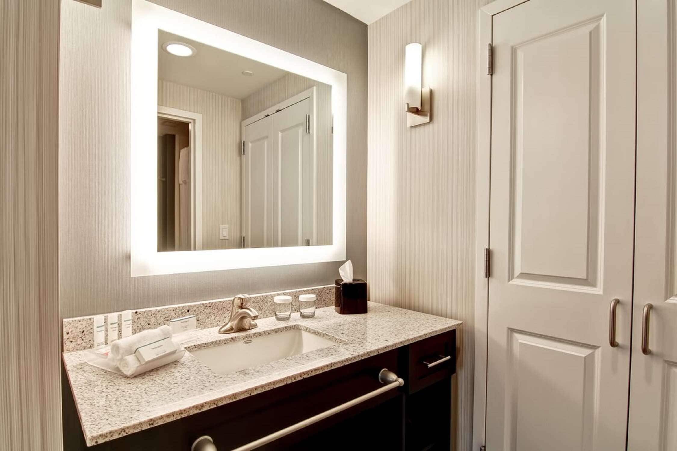A modern bathroom with a large mirror, a sink, and a towel rack.