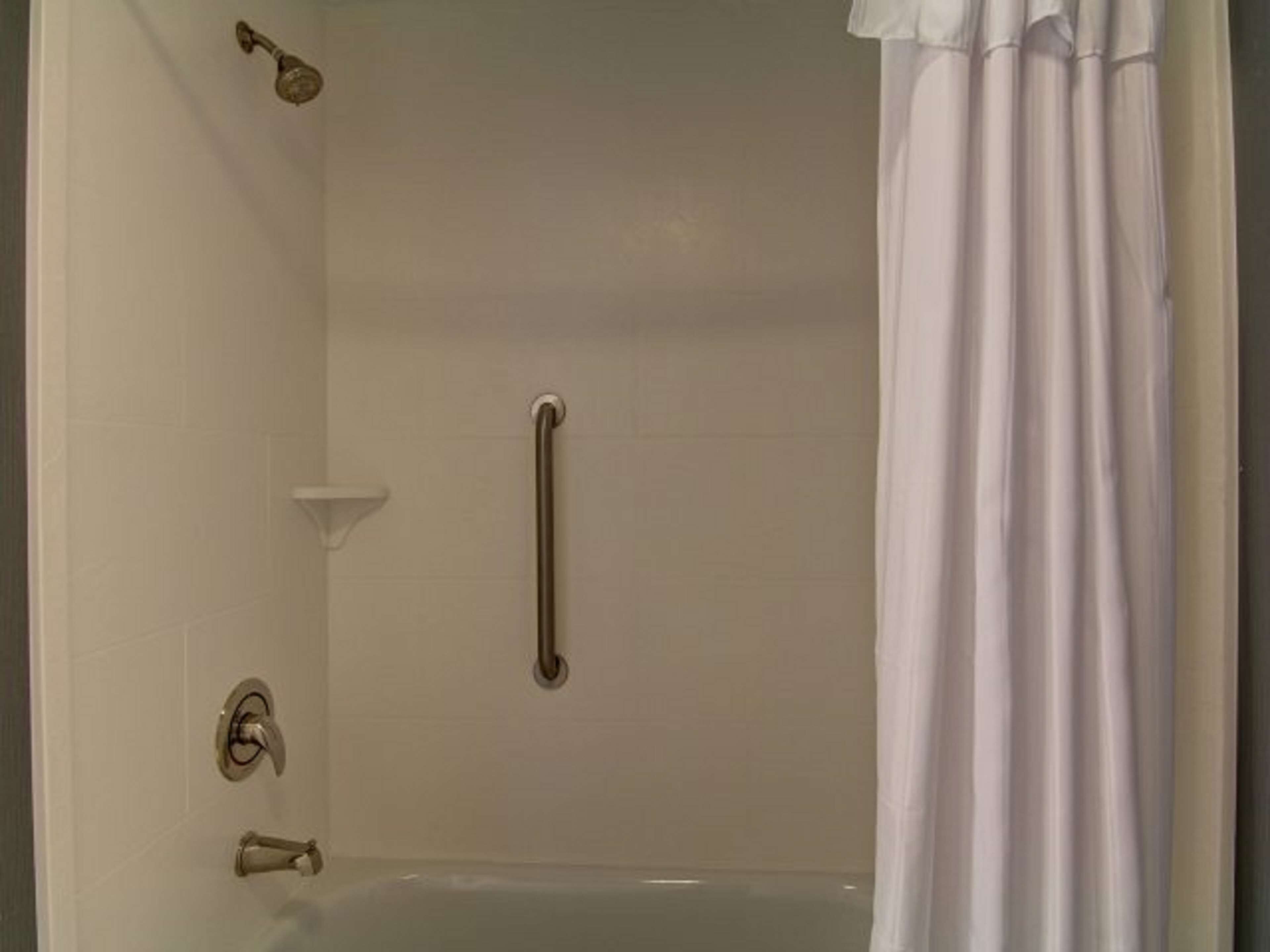 Une salle de bain équipée d’une baignoire, d’une barre d’appui et d’un pommeau de douche.