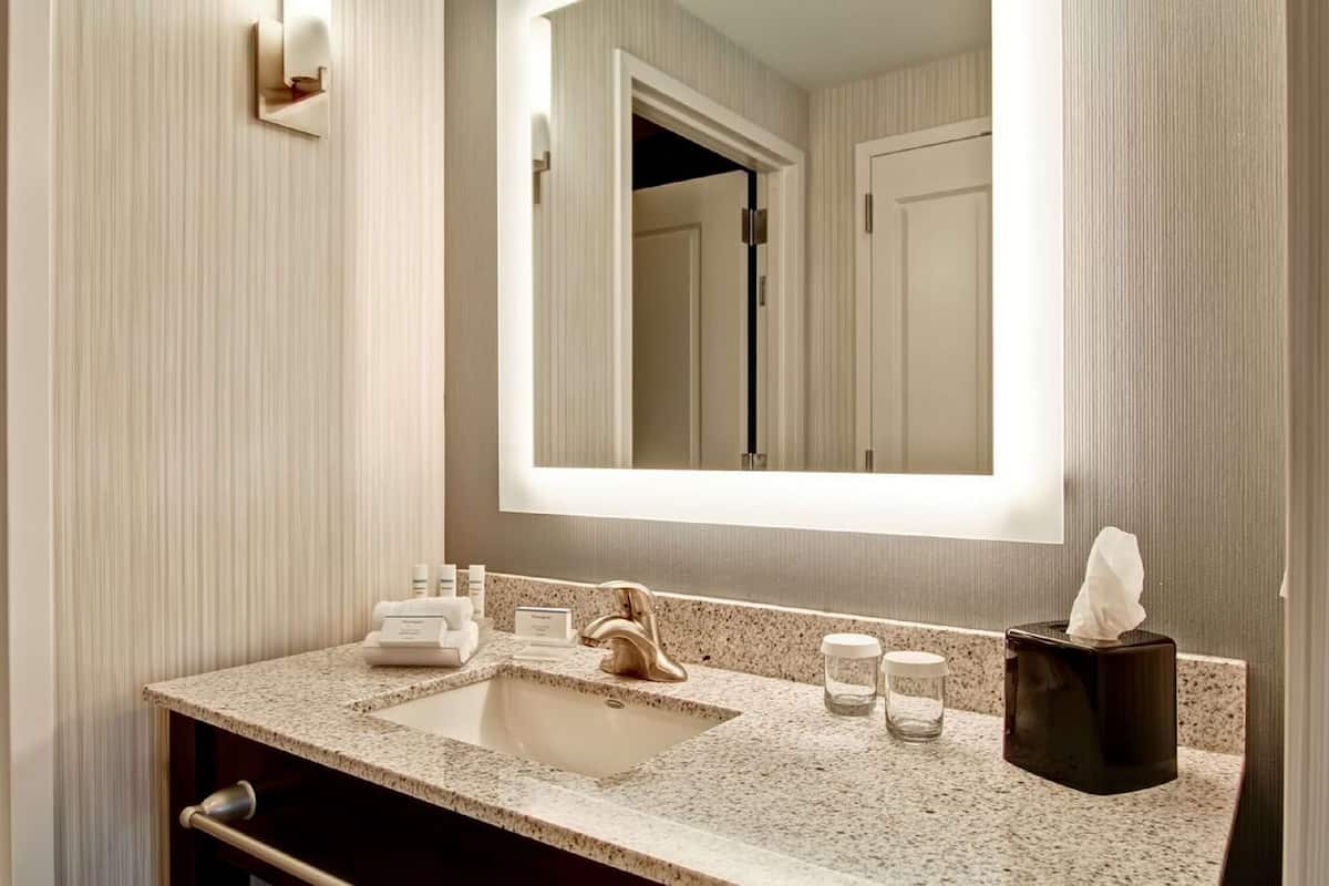 Une salle de bain dotée d’un comptoir en granit, d’un lavabo, d’un miroir et d’un distributeur de serviettes.