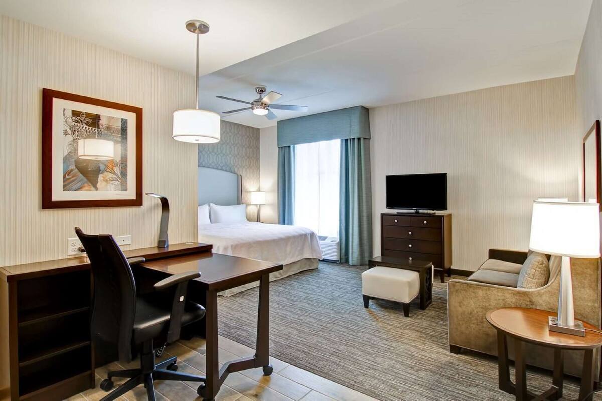Une chambre d’hôtel équipée d’un lit, d’un bureau, d’un fauteuil de bureau, d’un fauteuil, d’une télévision et d’un ventilateur de plafond.
