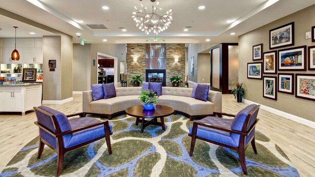 A modern lobby with a sectional sofa, two armchairs, a coffee table, and a fireplace. - Homewood Suites by Hilton Clifton Park (Clifton Park)