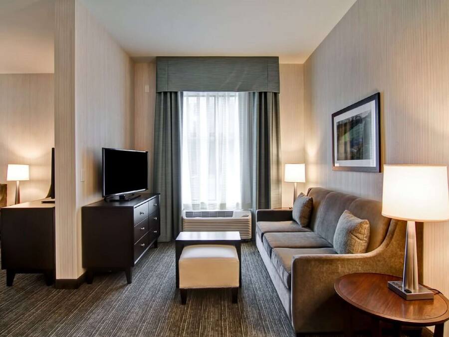 Hotelkamer met een flatscreen televisie, een bank, een klein tafeltje, een bureau en een raam met gordijnen.