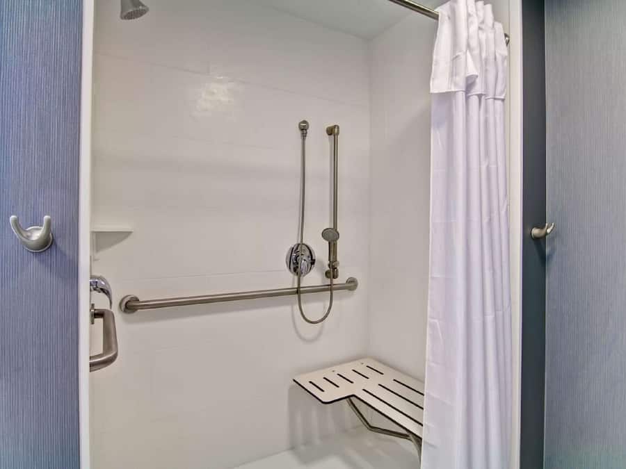 A shower area with a grab bar, a handheld showerhead, and a shower curtain.