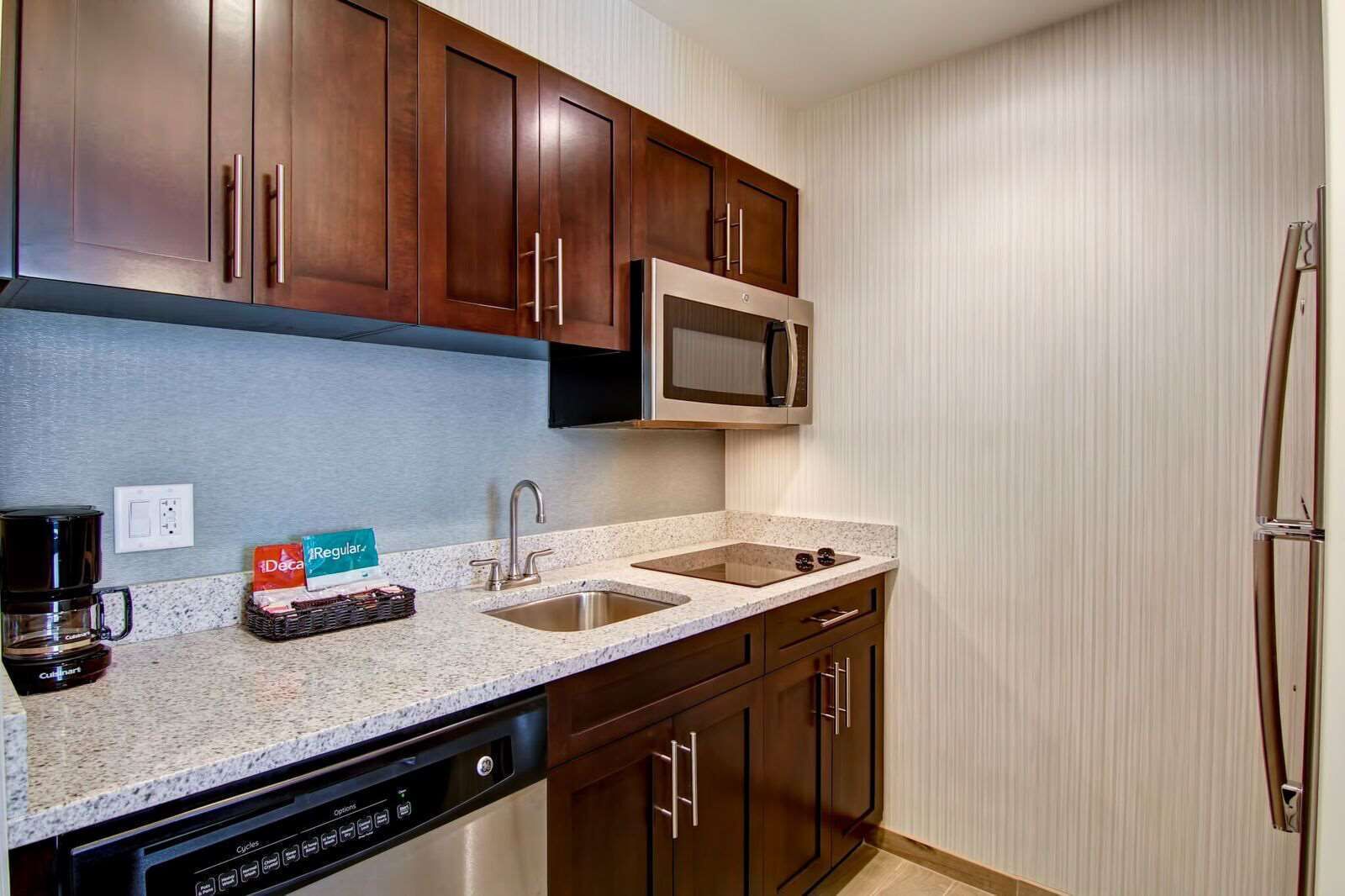 A modern kitchen with dark wood cabinets, a stainless steel sink, a microwave, and a dishwasher.