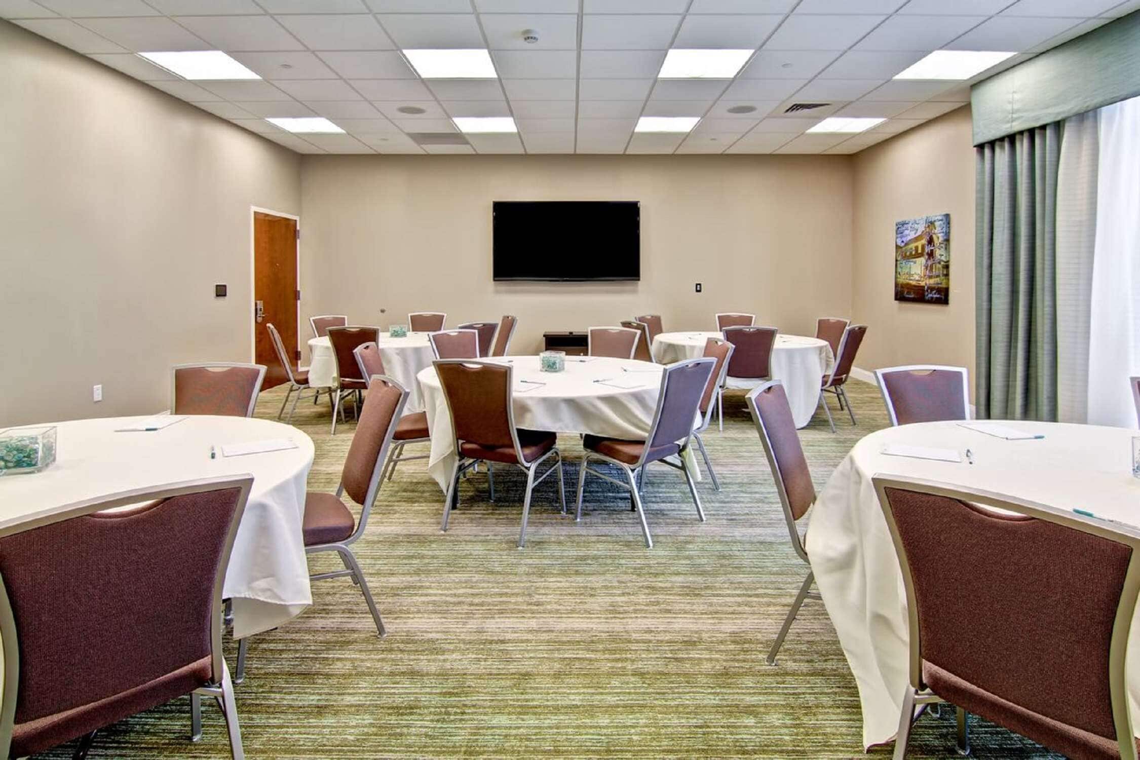 Une salle de conférence dotée de plusieurs tables et chaises, d’un grand téléviseur à écran plat et d’un sol recouvert de moquette.