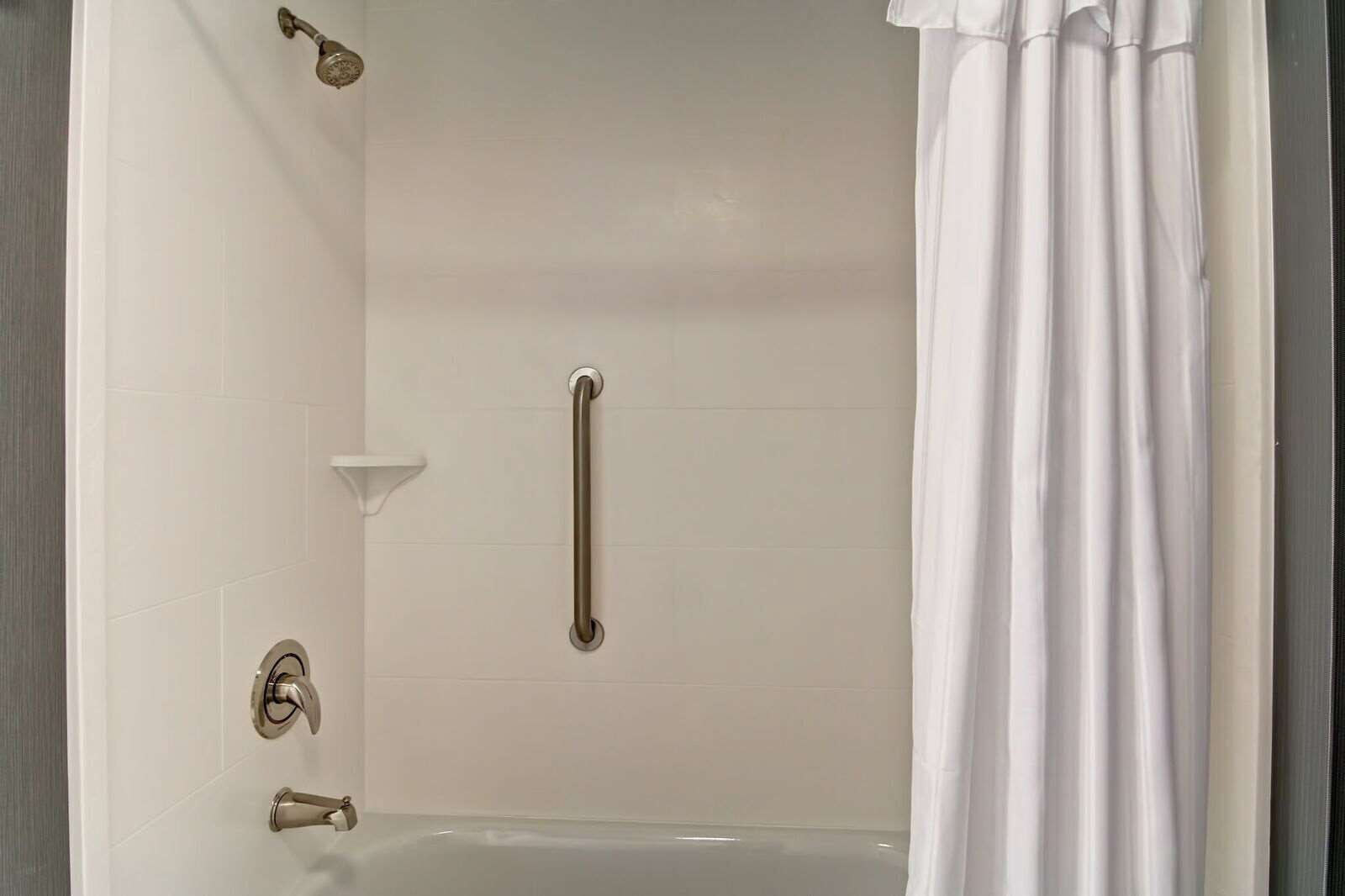 A bathroom with a bathtub, a shower, a grab bar, and a white curtain.