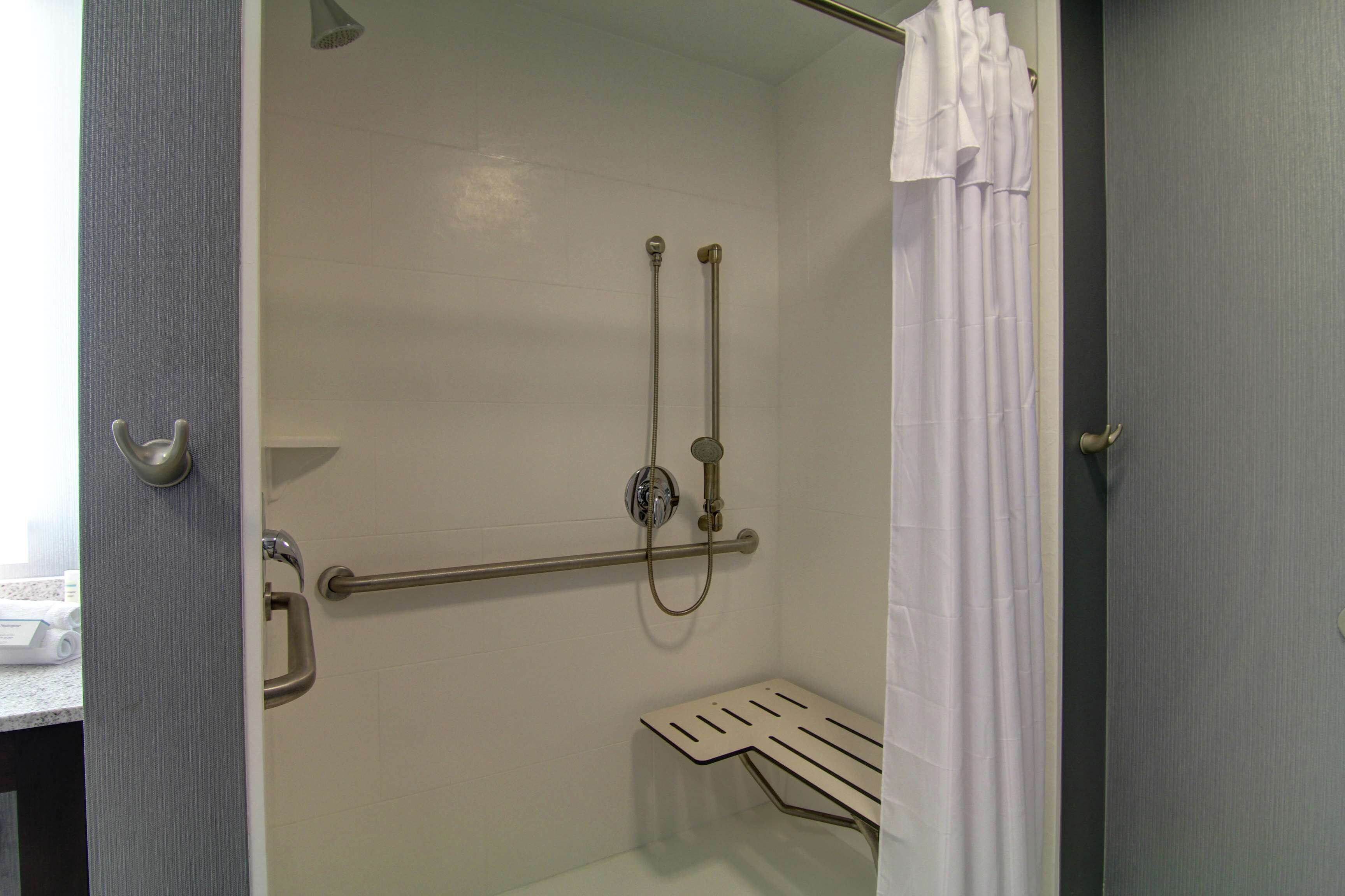 A shower area with a grab bar, a handheld showerhead, and a white shower curtain.