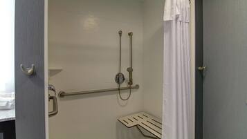 A shower area with a grab bar, a handheld showerhead, and a white shower curtain.