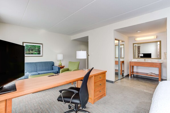 A hotel room with a wooden desk, a blue sofa, a television, a mirror, and a bed. - Hampton Inn & Suites Manchester (Manchester)