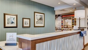 A hotel reception area with framed artwork on the wall, a sign for Hilton Honors, and a welcome sign for Manchester. - Hampton Inn & Suites Manchester (Manchester)