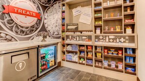 A snack and sundries section with a variety of packaged snacks, a refrigerated display, and a sign welcoming visitors to Manchester. - Hampton Inn & Suites Manchester (Manchester)