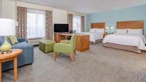 A hotel room with a bed, a desk with a TV, a sofa, and a chair. - Hampton Inn & Suites Manchester (Manchester)