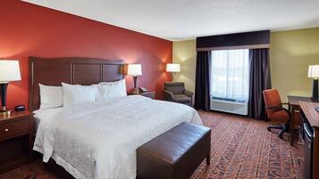 Una habitación de hotel con una cama grande, dos mesitas de noche con lámparas, una silla, un escritorio y una ventana con cortinas.