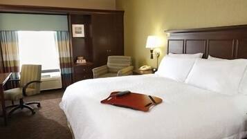 A hotel room with a large bed, a desk with a chair, a lamp, and a window with curtains.
