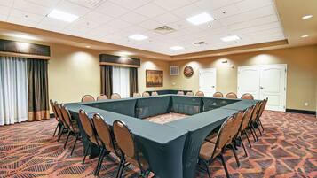 A conference room with a large rectangular table surrounded by chairs, a patterned carpet, and a ceiling with recessed lighting.