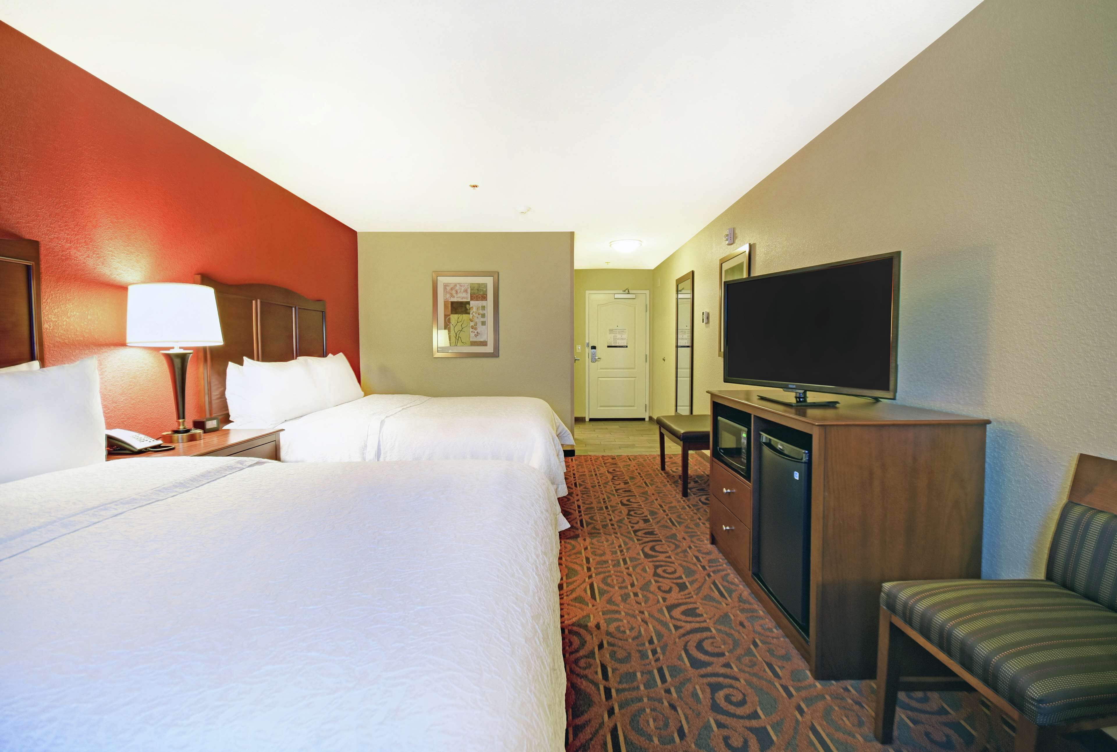 A hotel room with two beds, a desk with a television, a chair, and a carpeted floor.
