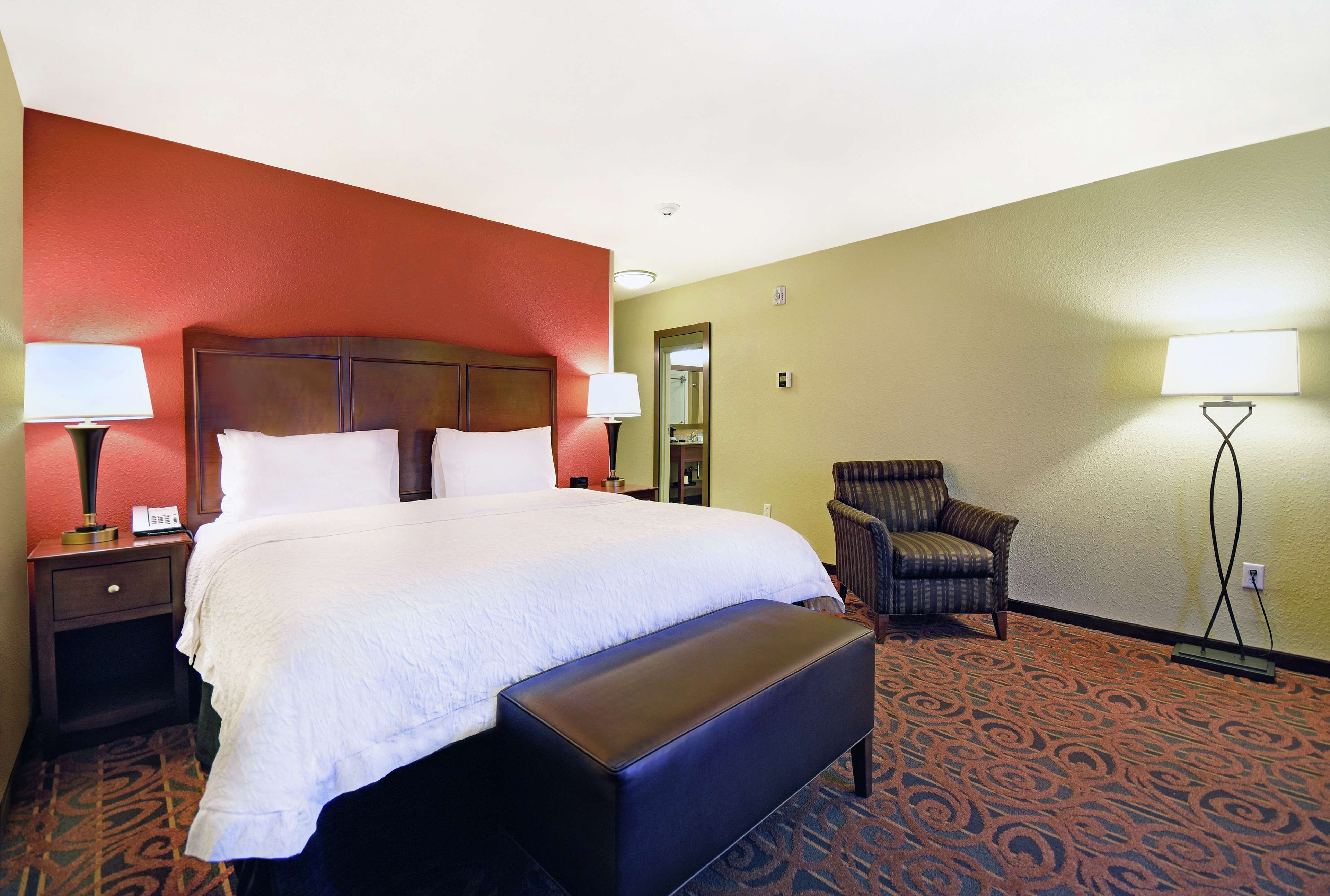 A hotel room with a large bed, a bench, a chair, and two bedside tables with lamps.
