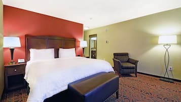 A hotel room with a large bed, a bench, a chair, and two bedside tables with lamps.
