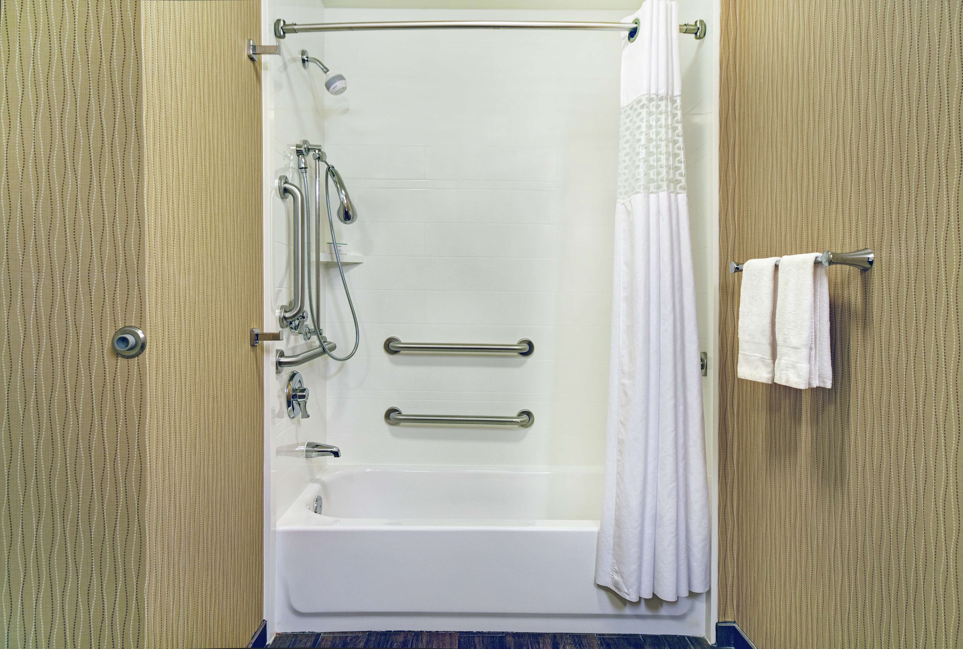 A standard hotel bathroom with a bathtub, grab bars, a towel rack, and a shower curtain.
