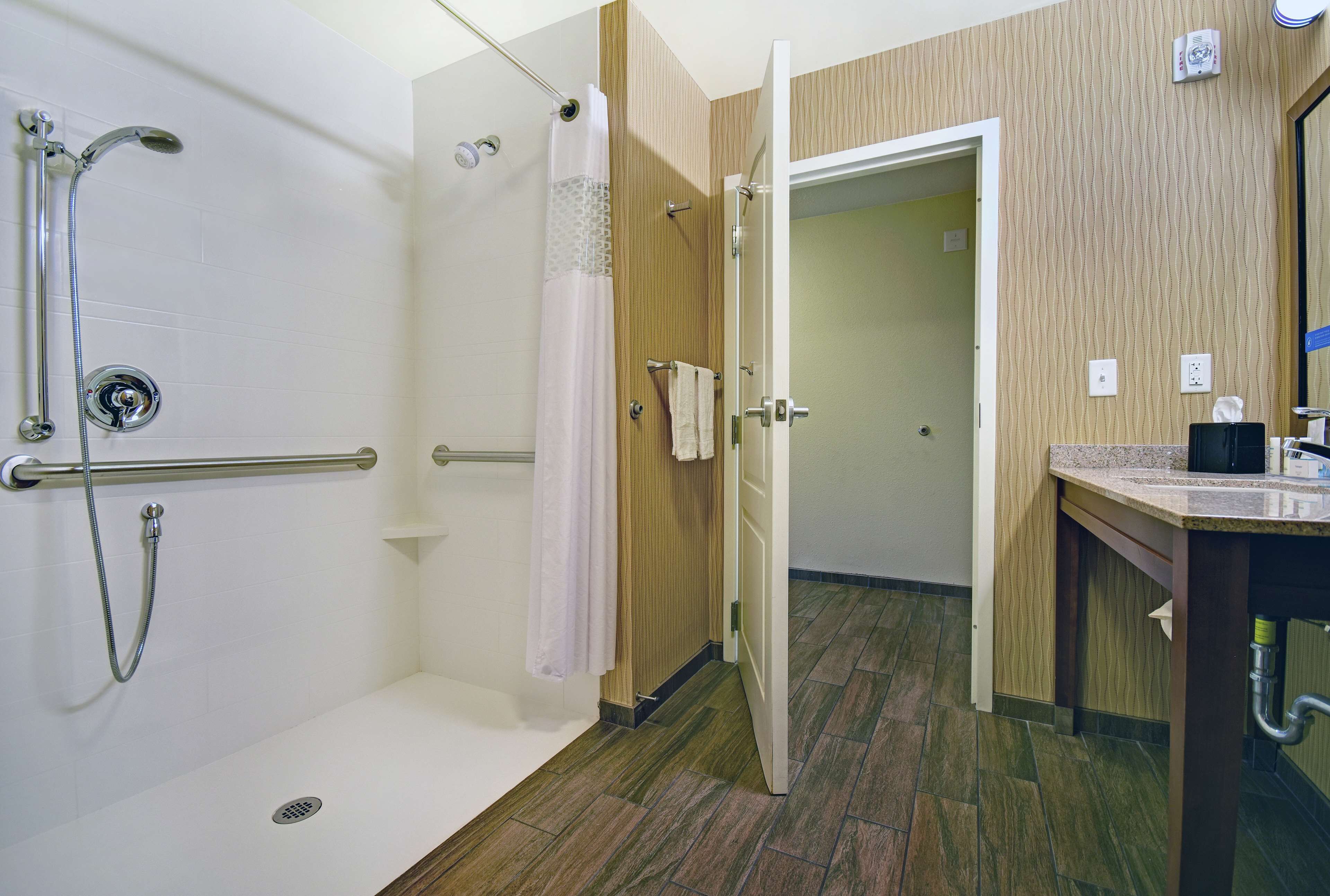 Zona de ducha con barra de apoyo, toallero y pared de paneles de madera.