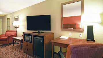 A hotel room with a television, a desk, a chair, a microwave, and a small refrigerator.