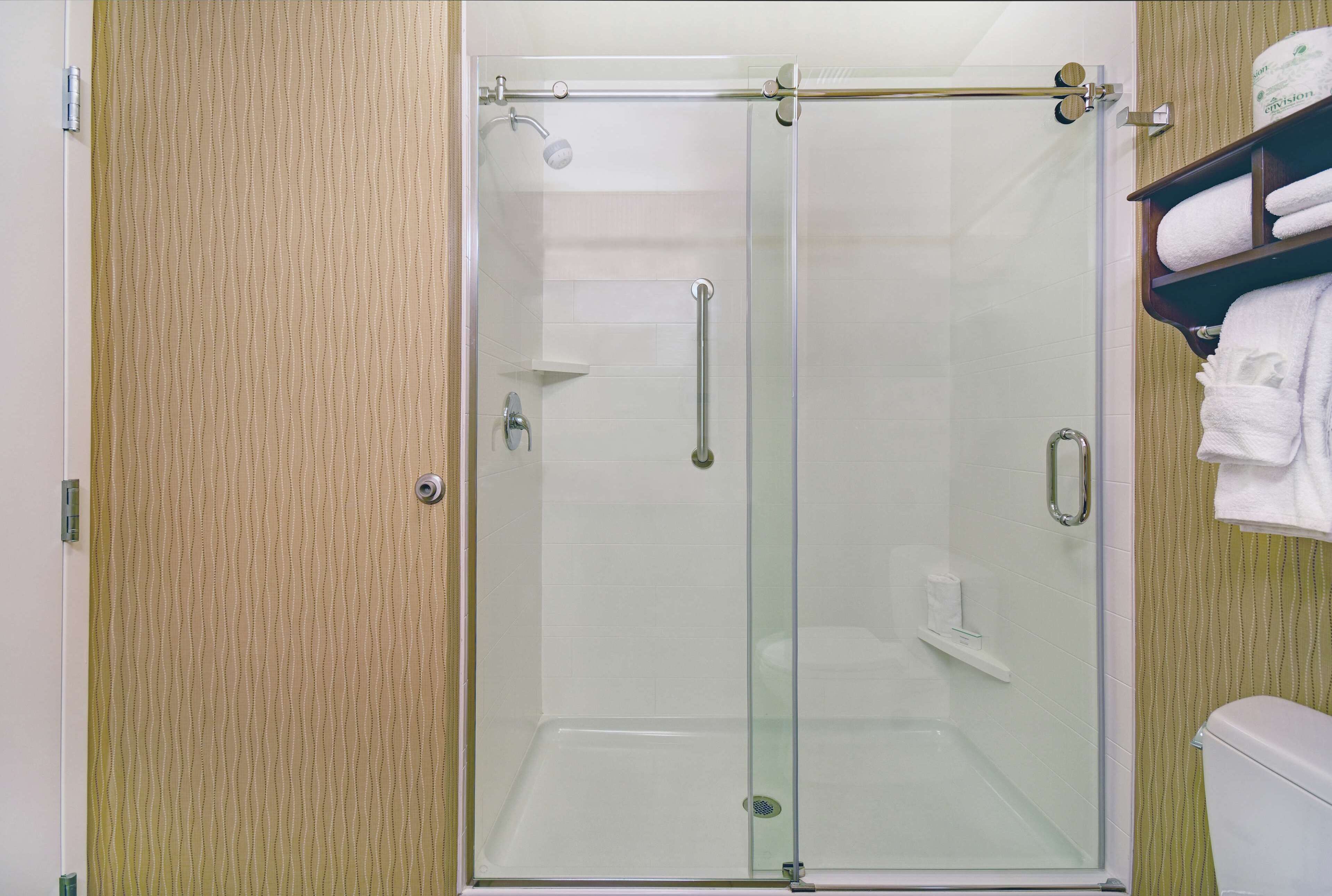 A glass-enclosed shower stall with a towel rack and a toilet visible to the right.