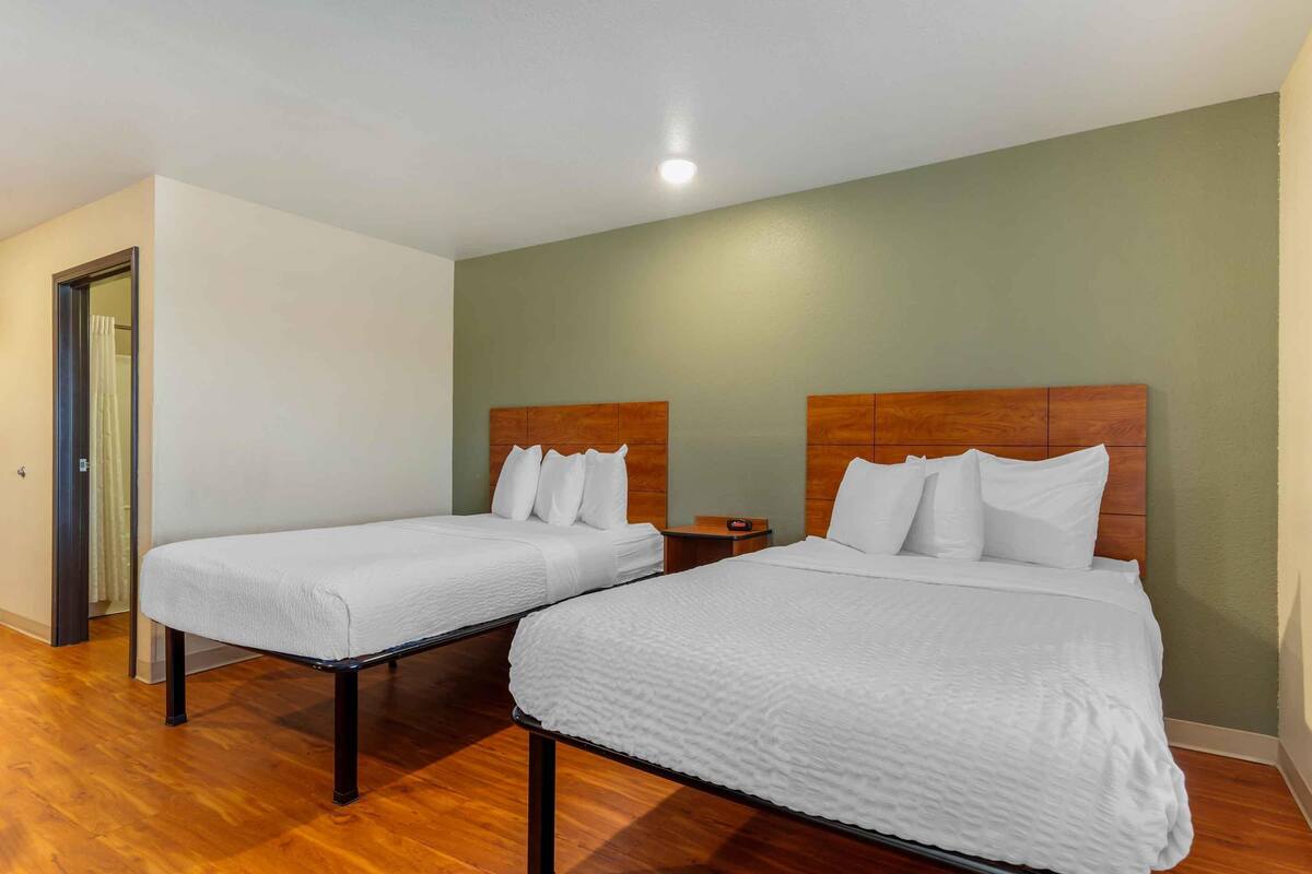 A hotel room with two beds, wooden headboards, and a small bedside table.