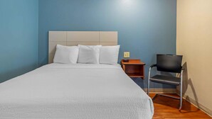 Une chambre d’hôtel avec un grand lit, une table de chevet en bois, une chaise moderne et un mur bleu.