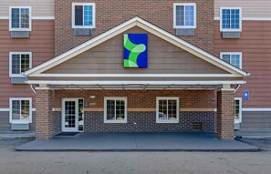 A building with a brick facade, a covered entrance, and a blue and green abstract artwork above the door. - Extended Stay America Select Suites - Atlanta - Chamblee (Chamblee)
